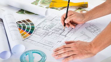 Close Up Of A Male Architect Drawing Plan Over Blueprints At Desk