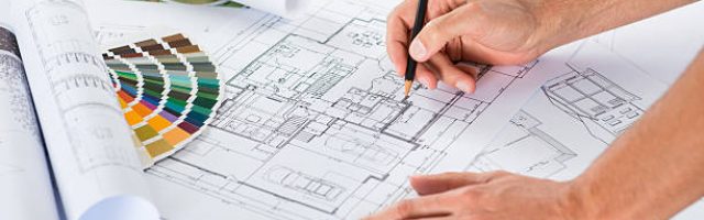 Close Up Of A Male Architect Drawing Plan Over Blueprints At Desk