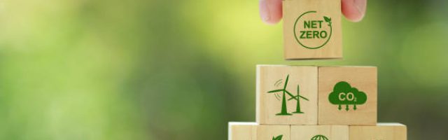Net zero and carbon neutral concept. Hand puts wooden cubes with netzero icons - renewable energy, co2 emissions reduction, green production, waste recycling.in green background